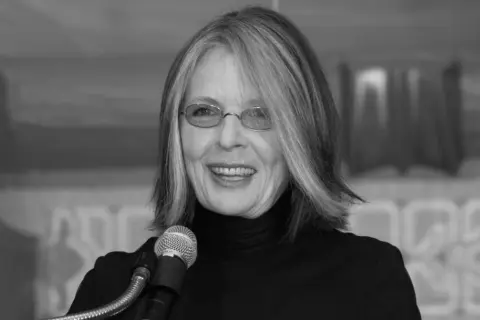 Diane Keaton w okularach i czarnym golfie, uśmiechnięta przy mikrofonie. Jej życie prywatne jest inspiracją dla wielu.