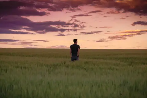 Ein Mann steht in einem weiten Feld, blickt in den dramatischen Himmel. Ein Moment der stillen, **contemplative deutsch** Reflexion.