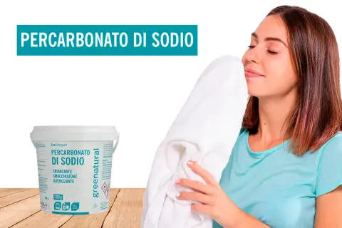 Donna annusa un candido asciugamano, felice del profumo fresco. Accanto, un barattolo di Percarbonato di Sodio, smacchiatore naturale per lavatrice.