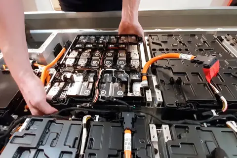 Manos trabajando en el interior de un paquete de baterías de coche eléctrico. Averiguar cuanto cuesta cambiar la bateria del coche es clave.