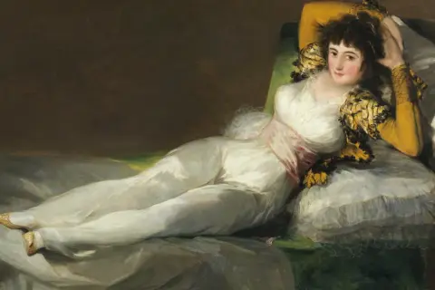 La venus del espejo, una mujer recostada en un diván, viste un traje blanco y mira al espectador con una expresión seductora.