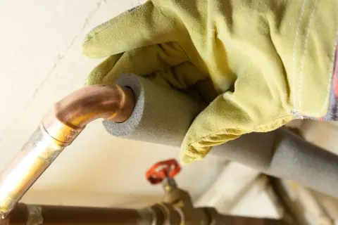 Mit gelben Handschuhen werden Heizungsrohre isoliert, um Energie zu sparen.