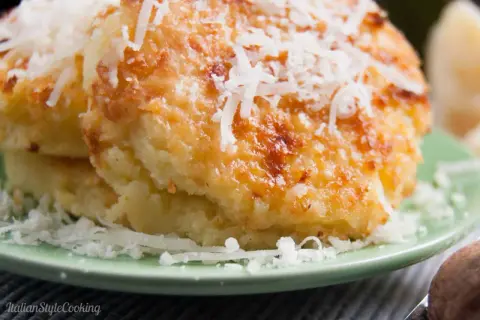 Gebackene Gnocchi alla Romana, goldbraun und mit geriebenem Parmesan bestreut, auf einem grünen Teller.