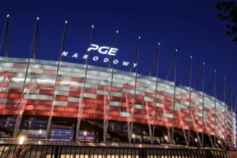 PGE Narodowy nocą, oświetlony w barwach narodowych. Imponująca pojemność stadionu robi wrażenie.