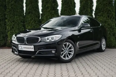 Eleganckie, czarne BMW GT lśni na tle zielonych drzew.