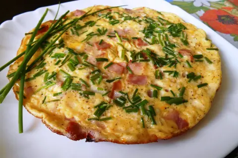 Puszysty omlet ze szczypiorkiem i kawałkami wędliny, podany na białym talerzu.