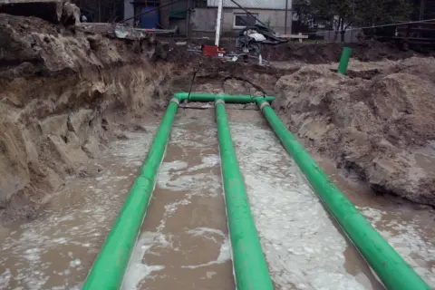 Trzy zielone rury tworzą gruntowy wymiennik ciepła w wykopie.