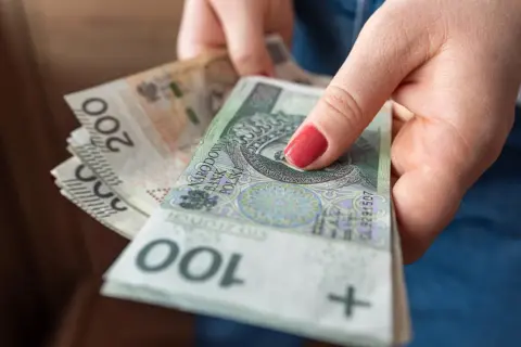 Dłonie trzymają stos polskich banknotów 100 i 200 zł. Może to być przygotowanie do przelewu podatkowego lub innej płatności.