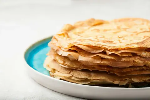 En hög med gyllene pannkakor, gjorda med vatten istället för mjölk, ligger på en blå och vit tallrik.
