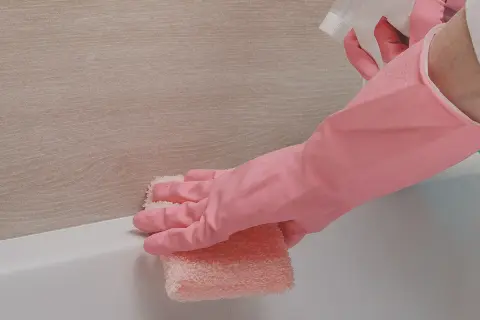 Main rose, une éponge rose nettoie le joint silicone jauni de la baignoire.