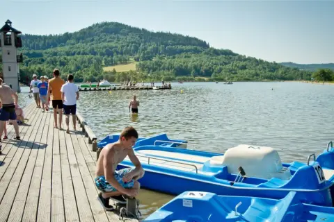 Letnie popołudnie nad jeziorem, gdzie można podziwiać śląskie atrakcje. Ludzie spacerują po molo, pływają i relaksują się przy wodzie.