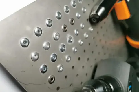 Metalowa blacha z rzędem nitów zrywanych i narzędziem do ich montażu.