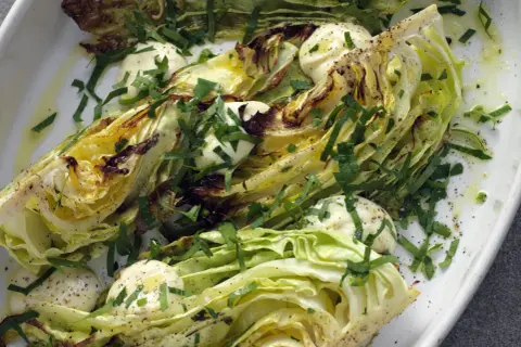 Ugnsbakad vitkål, skuren i klyftor, serverad med en krämig dressing och färska örter. En enkel men smakrik rätt.