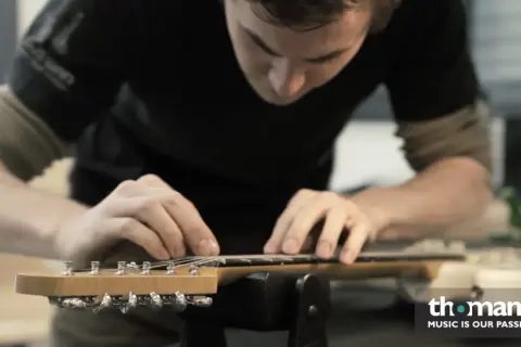 Ein Mann arbeitet an der bund gitarre. Er justiert die Saiten mit seinen Fingern.