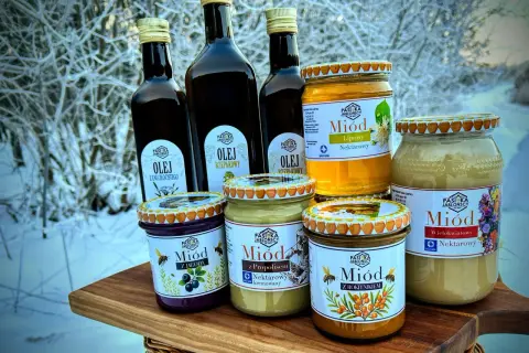 Słoiki z miodem i butelki z olejem na tle zimowego krajobrazu. Miód pitny trójniak ile procent? Sprawdź etykiety!