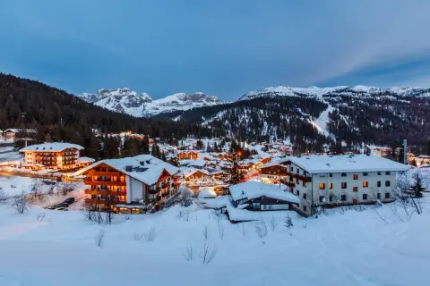 Paesaggio innevato di Madonna di Campiglio al crepuscolo. Hotel illuminati e montagne sullo sfondo, un invito a scoprire cosa vedere.