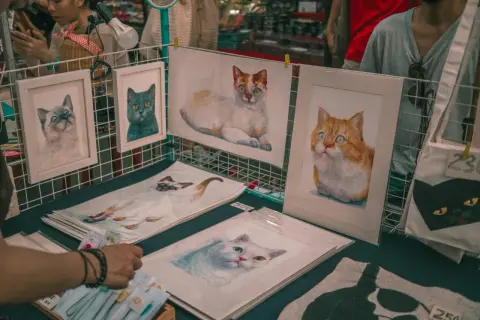 Des tableaux de chats, des portraits de félins aux regards expressifs, comme les chats Baudelaire, sont exposés sur un étal.