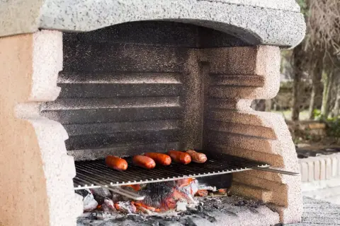 Prosty murowany grill z cegły, na którym pieką się kiełbaski nad żarem.