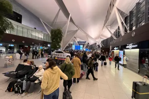Tłum ludzi w terminalu lotnisko gdańsk odloty. Wszyscy czekają na swoje podróże, niektórzy siedzą, inni idą z bagażami.