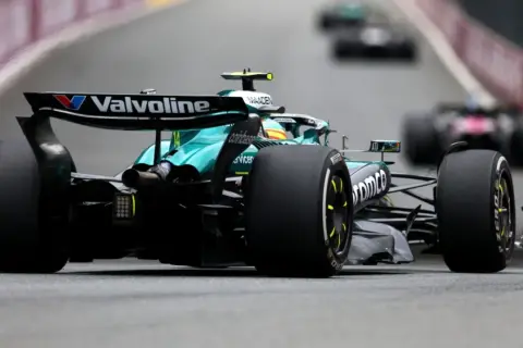 Un coche Aston Martin F1 verde compite en la pista, con otros coches borrosos detrás.