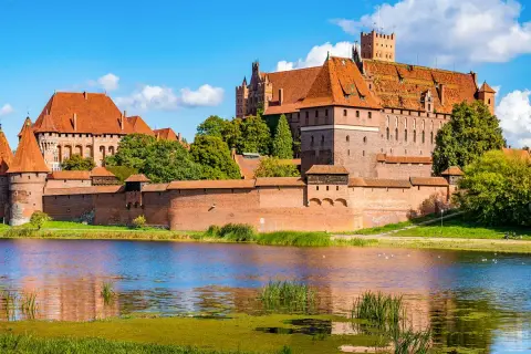 Die imposante Marienburg Burg, eine mittelalterliche Festung aus rotem Backstein, thront über einem ruhigen See.