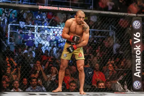 Jose Aldo, en ikonisk MMA-fighter, står i buren, redo att utöka sitt imponerande jose aldo record. Publiken jublar bakom nätet.