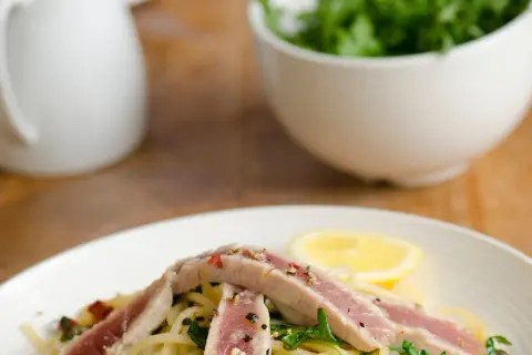 Un piatto di spaghetti con tonno fresco, rucola, capperi e una fetta di limone.