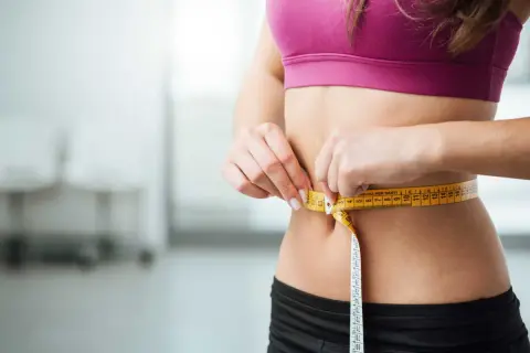 Une femme mesure sa taille avec un mètre ruban. La question "peut on maigrir sans sport" est au cœur de cette image de perte de poids.