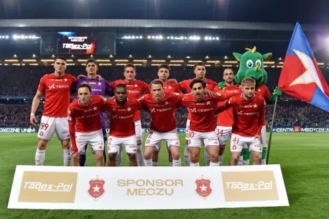 Piłkarze Wisły Kraków w czerwonych strojach, z maskotką i flagą. Najnowsze wisła kraków aktualności.