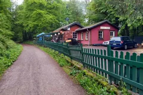 Der Weg zum Bahnhof Burgholz führt vorbei an einer roten Gaststätte mit grünen Zäunen und Autos.