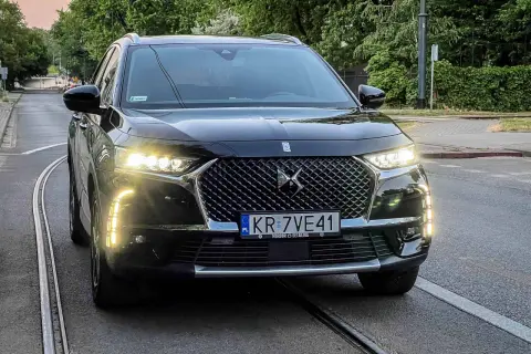 Czarny DS 7 z włączonymi światłami dziennymi stoi na torach tramwajowych.
