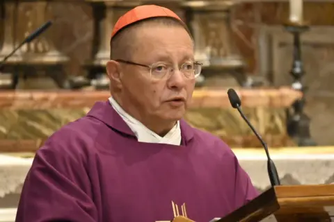 Biskup Ryś, w purpurowej szacie i z czerwoną piuską, przemawia przy mikrofonie, dzieląc się swoimi poglądami.