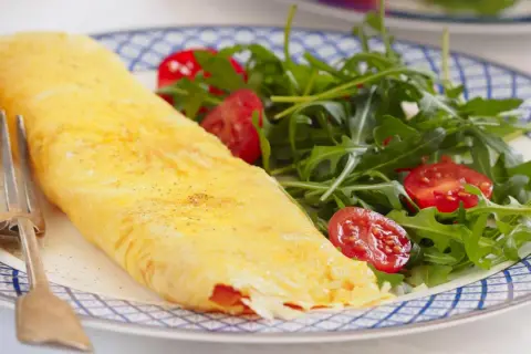Tortilla francesa rellena, dorada y esponjosa, servida con una fresca ensalada de rúcula y tomates cherry. Un bocado delicioso y saludable.