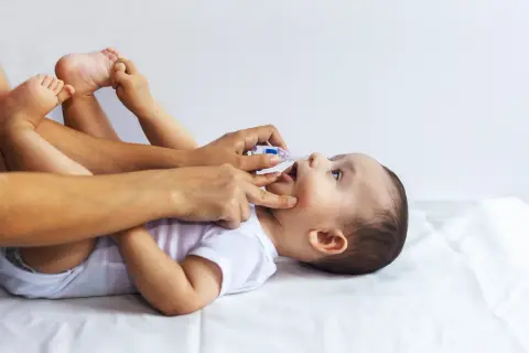 Dłoń podaje sól fizjologiczną do noska niemowlęcia leżącego na plecach.