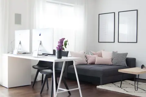 Ein helles Arbeitszimmer mit Schreibtisch, zwei Computern und einem gemütlichen Sofa, das zum Einrichten einlädt.