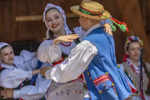 Para tańczy w tradycyjnych strojach ludowych, celebrując muzykę folkową.