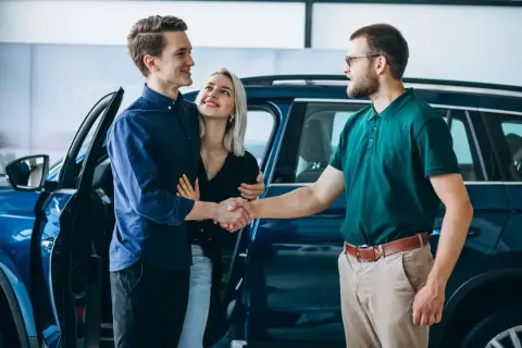 Para młoda uśmiecha się, ściskając dłoń sprzedawcy przy nowym aucie. To ich wymarzony auto w leasing dla osoby prywatnej.