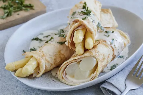 Pfannkuchen mit Spargel und Schinken, übergossen mit einer cremigen Sauce und garniert mit Petersilie.