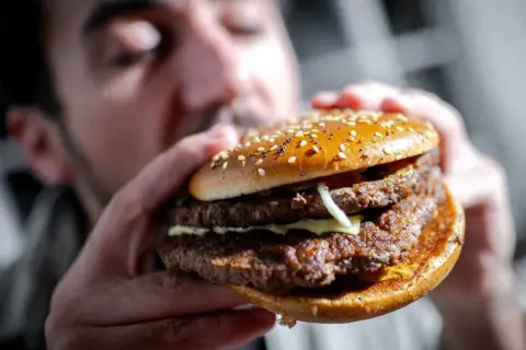 Mann hält einen saftigen Doppel-Cheeseburger mit Sesambrötchen. Perfekt für Burger Rezept Ideen!