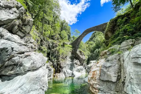 Idyllische Schlucht mit Steinbrücke, ideal für Tessin Wandern. Türkisgrünes Wasser fließt zwischen Felsen.