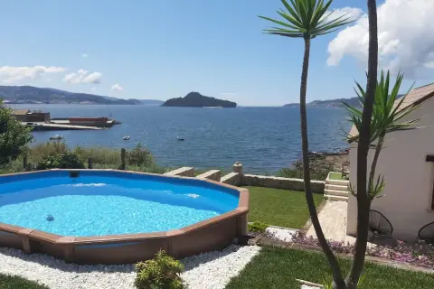 Piscina azul con vistas al mar y a la playa de Limens. Palmeras y césped verde rodean la zona de descanso.