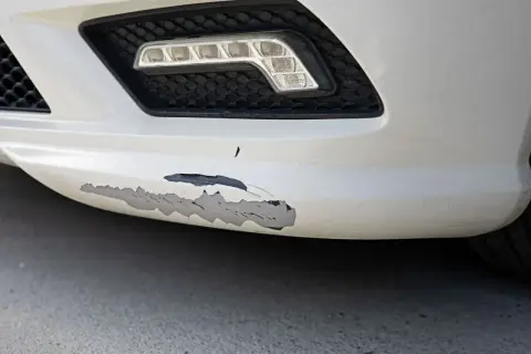 Zderzak z widocznym, zdartym lakierem w kilku miejscach. Widać czarny podkład pod białym lakierem.