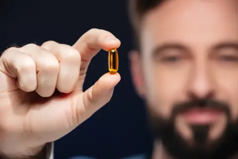 Mężczyzna trzyma kapsułkę omega-3. Lekarze potwierdzają jej pozytywny wpływ na zdrowie.