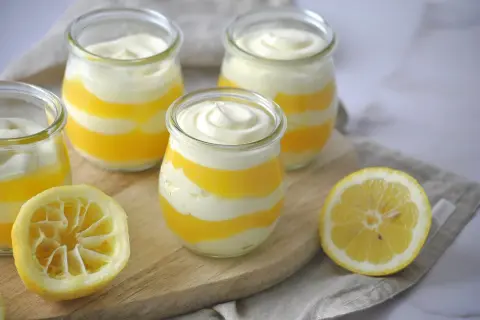 Schichtdessert in Gläsern, perfekt, wenn Sie Zitronenmelisse Creme selber machen möchten. Frische Zitronenhälften liegen daneben.