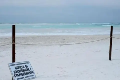 Spiagge bianche deserte con mare turchese. Un cartello vieta balneazione e stazionamento.
