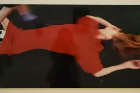 Boris Mikhailov cattura un momento di movimento sfocato: una donna in abito rosso e un piede con pallone da calcio.