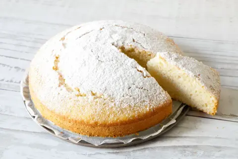 Una soffice torta all'acqua, cosparsa di zucchero a velo, con una fetta tagliata che ne mostra la morbidezza.