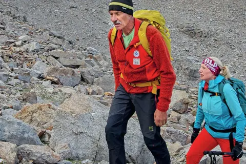 Simon Gietl und eine Frau wandern auf einem felsigen Berghang. Sie tragen Rucksäcke und Wanderkleidung.