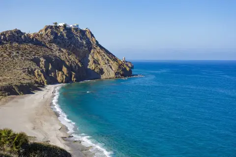Costa rocosa con una playa de arena dorada y aguas turquesas. En lo alto del acantilado, casas blancas y un faro vigilan la costa. Un lugar idílico para disfrutar del sopalmo playa.