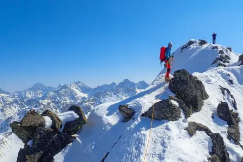 Wspinaczka na Orlą Perć zimą. Dwóch alpinistów na ośnieżonym szczycie, jeden z nich asekurowany liną.
